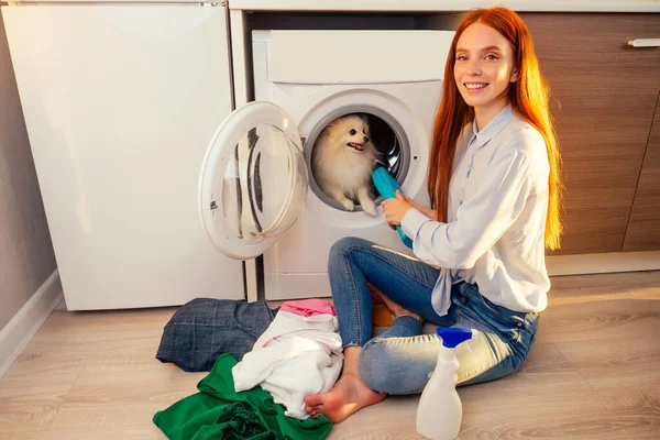 Fie, what stench Shocked excited redhaired girl wash pile of dirty smelly clothes ,her adorable fluffy spitz helpinh inside the washing machine at home — Foto Stock