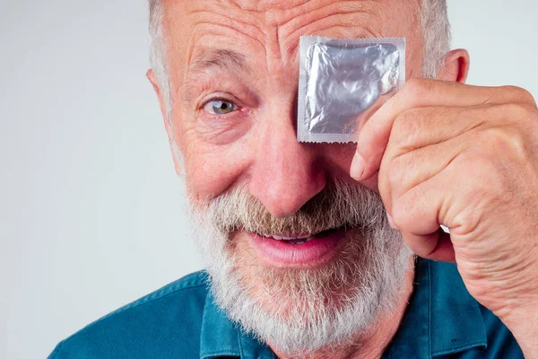 Старый кавказский мужчина держит упакованный резиновый латексный презерватив на белом фоне студии — стоковое фото
