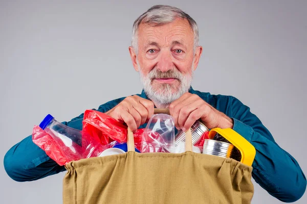 Vieux grand-père tenant sac écologique en coton plein d'ordures en studio fond blanc — Photo