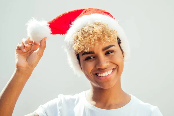 Afrikansk amerikansk flicka med snö-vitt leende och lockigt blont hår bär röd hatt, tittar på kamera i studio vit bakgrund — Stockfoto