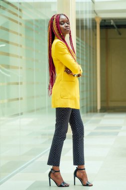 Yaratıcı stilisti Afro-Amerikalı, Kanekalon saçlı, sarı ceketli, uzun afro örgülü genç bir kadın. Güzel giysi tasarımcısı zanaat atölyesinde poz veriyor.