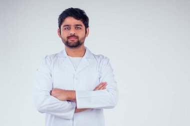 Beyaz ceket giyen yakışıklı hindi adam doktor kollarını göğsüne kavuşturdu ve stüdyonun arka planındaki kameraya baktı.