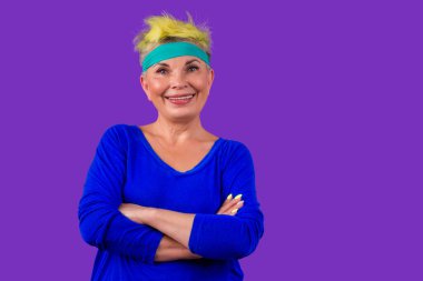 Stüdyo menekşe arka planında gülümseyen pilates eğitiminden sonra alnında mavi bandajla şık sarı boyalı saçları olan mutlu, aktif emekli bir kadın. Sonsuza dek genç ruhlu.