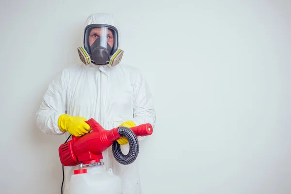 Böcek ilaçlama işçisi. Apartman fotokopi makinesine böcek ilacı sıkıyor. Beyaz duvarlar arka planda.