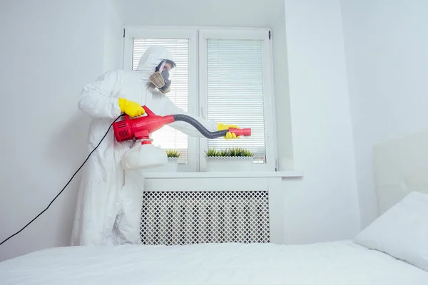 Работник по борьбе с вредителями лежит на полу и распыляет пестициды в спальне — стоковое фото