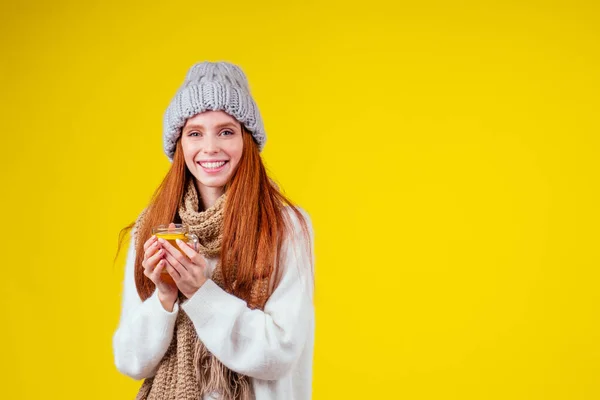 Sjukdom rödhårig ingefära kvinna snygg klädd stickad tröja och hatt med halsduk dricka varmt te kopp med citron i studio gul bakgrund — Stockfoto