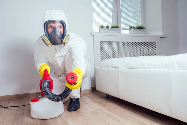 Pest control worker lying on floor and spraying pesticides in bedroom — Stock Photo, Image