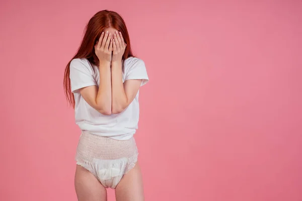 Młody zdumiony i zaskoczony rudowłosy rude kobieta noszenie pieluchy nietrzymanie moczu w studio różowy tła.uczucie wstydu i wstydu — Zdjęcie stockowe