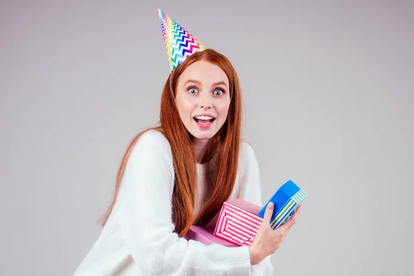 Rothaarige Ingwerfrau trägt Geburtstagskappe Horn hält viele Geschenkboxen im Studio weißen Hintergrund — Stockfoto