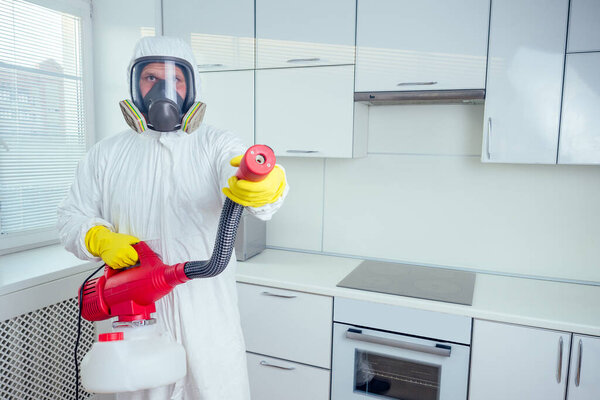 pest control worker standing with sprayer in kitchen