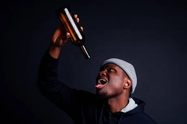 アフリカ系アメリカ人のグレーの帽子とフード付きの瓶を身に着けているアフリカ系アメリカ人です黒の背景にワインと。アルコール依存症ホームレスのアルバムコンセプト — ストック写真