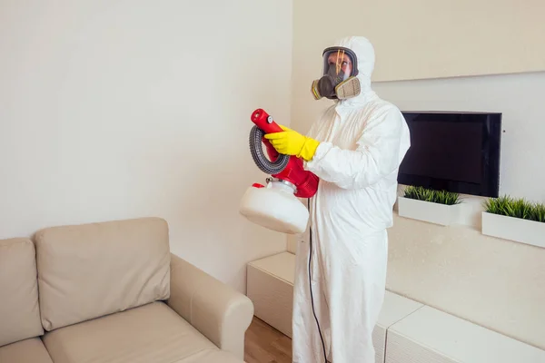 Travailleur de la lutte antiparasitaire en uniforme pulvérisation de pesticides sous le canapé dans le salon — Photo