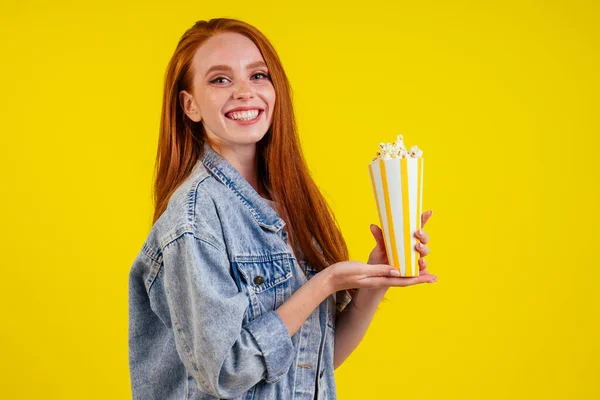 Emotionella tankeväckande kalorier rödhårig ingefära kvinna bär jeans jacka och hålla popcorn i studio gul bakgrund — Stockfoto