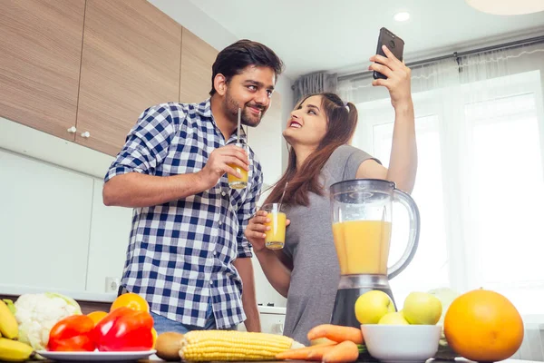 healthy and eco lifestyle.happy indian woman with her husband making smoothie in big kitchen,taking photos portrait on smartphone camera