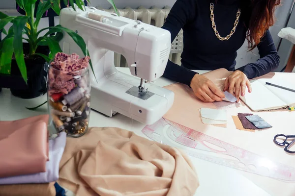 Bela costureira com cabelo longo escreve em um caderno. o alfaiate cria uma coleção de roupas. jovem mulher roupas de grife trabalhando com couro — Fotografia de Stock