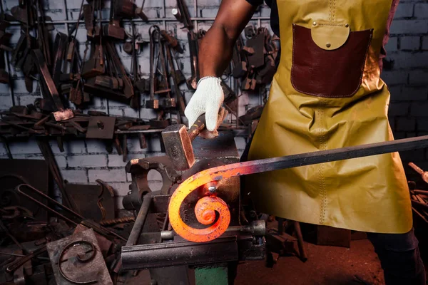 Jóképű afro-amerikai kovács férfi munkás dolgozik műhelyben, visel bőr kötény — Stock Fotó