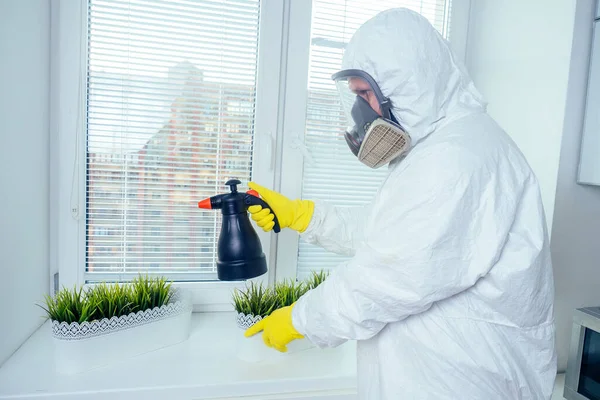 Εργάτης καταπολέμησης παρασίτων με ομοιόμορφο ψεκασμό φυτοφαρμάκων κάτω από το ντουλάπι στο λουλούδι κουζίνας στο παράθυρο — Φωτογραφία Αρχείου