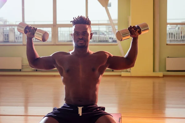 Afro memegang latihan dumbbells untuk abc press dan tangan di jendela gym latar belakang — Stok Foto