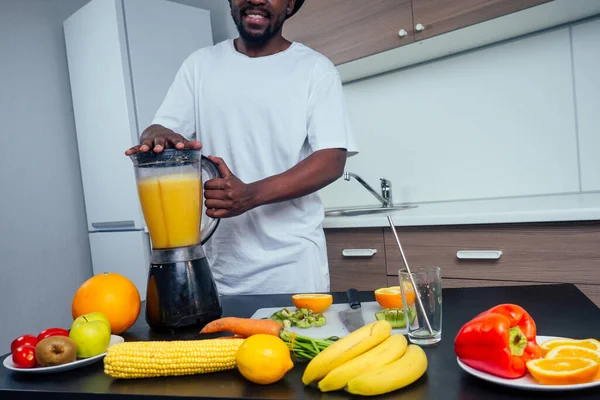Hombre africano joven y guapo haciendo un batido para el desayuno usando una licuadora en casa — Foto de Stock