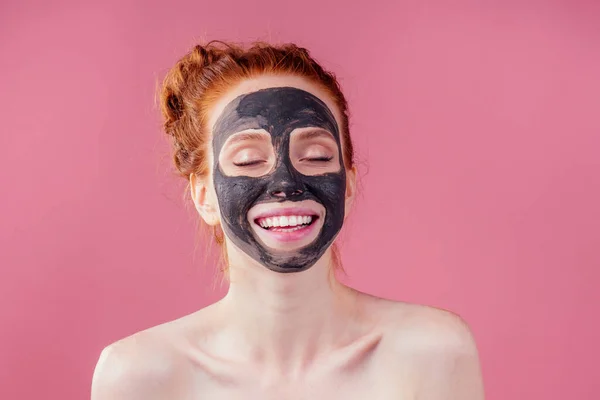 Rudowłosy rude nastolatek dziewczyna z czarny gliny maska na jej ładna twarz na różowy studio tło — Zdjęcie stockowe