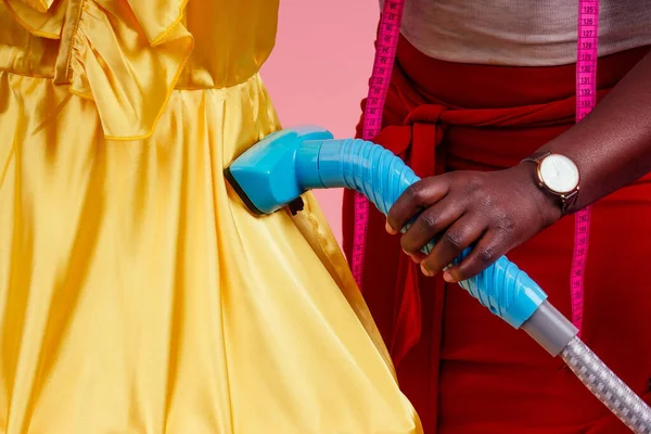 ドライクリーニングサロン、スタジオピンクの背景にシルク赤と黄色のドレスのための蒸気装置ホット蒸気発生器を保持アフリカ系アメリカ人の仕立てドレスメーカー — ストック写真