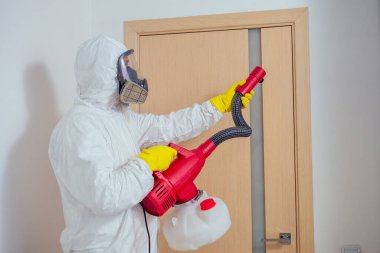 Haşere kontrol görevlisi yerde yatıyor ve yatak odasına böcek ilacı sıkıyor.