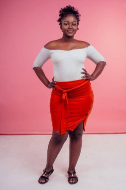 Tam boy portre güzel artı boy model beyaz bluz ve kırmızı seksi etek giyiyor stüdyo pembe arka planda poz veriyor.