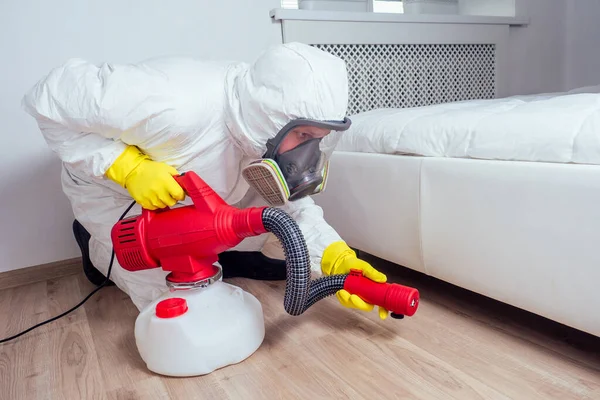 Disinfestatore sdraiato sul pavimento e spruzzando pesticidi in camera da letto — Foto Stock