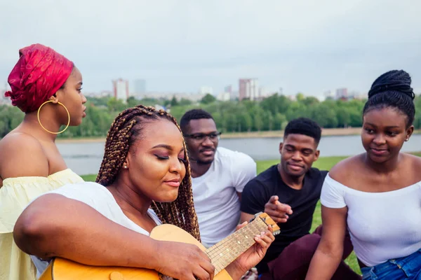 Group of smiling happy afro-american friends friends playing guitar outdoors picnic in the campaign — Stock Photo, Image