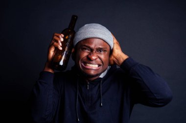 african american man holding a bottle of wine and feeling headache shit in studio black background.bum homeless drowning out the pain