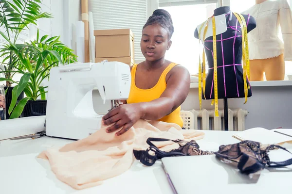 beautiful african american tailor woman sewing laces sexy lingerie in showroom