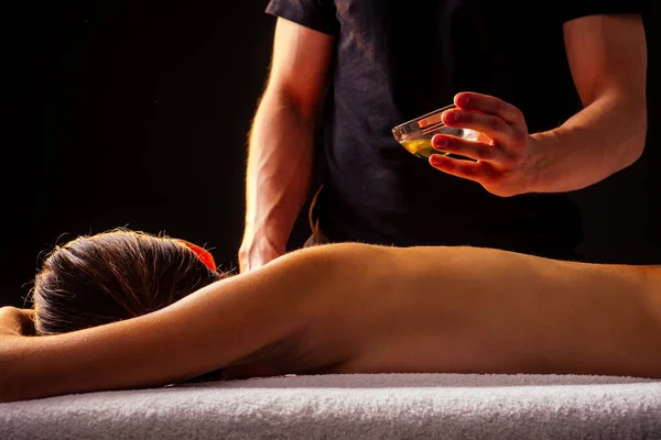 Młoda Hinduska kobieta leżąca na stole i coraz ajurwedyjski masaż z olejkiem organicznym lub miodem w ciemnym pokoju.massagist mężczyzna wylewa klienta z powrotem — Zdjęcie stockowe
