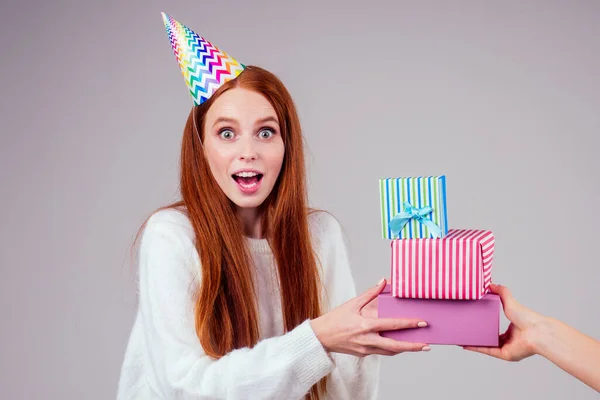 Rothaarige Ingwerfrau trägt Geburtstagskappe Horn hält viele Geschenkboxen im Studio weißen Hintergrund — Stockfoto