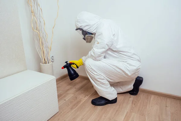 Lavoratore disinfestante in uniforme spruzzando pesticidi sotto il divano in salotto — Foto Stock