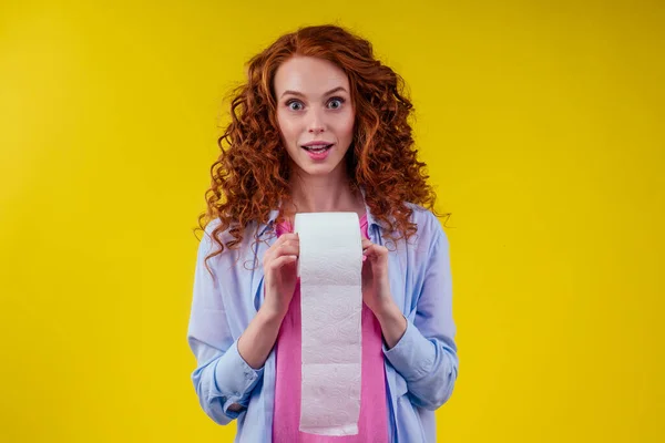 Schöne lockige rothaarige Ingwerfrau hält Toilettenpapierrolle auf gelbem Hintergrund — Stockfoto