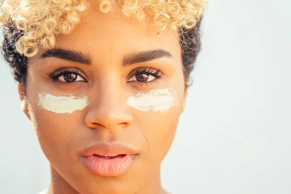 Concept rajeunissant et hydratant. femme brésilienne avec des boucles afro blondes appliquant de l'argile blanche sur une peau parfaite sur fond de studio blanc — Photo