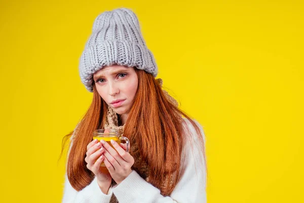 Sjukdom rödhårig ingefära kvinna dålig ser klädd stickad tröja och hatt med halsduk dricka varmt te kopp med citron i studio gul bakgrund — Stockfoto