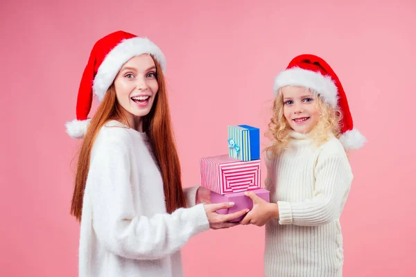 Få xmas presenter.flickor i röd tomte hatt hålla ett gäng presentförpackningar i studio rosa bakgrund — Stockfoto