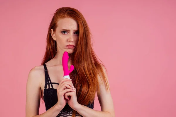 Frustrated beautiful redhaired ginger woman in sexy black linen lace holding vibro dildo and disappointment feeling in studio pink background — Φωτογραφία Αρχείου