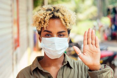 Koruyucu maskeli Afro kadın sokakta duruyor. Coronavirus konsepti