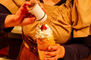 İştahlı bir kadın Prag caddesinde eko ahşap kaşık kullanarak vanilyalı ve çilekli geleneksel Çek tatlısı Trdelnik yiyor.