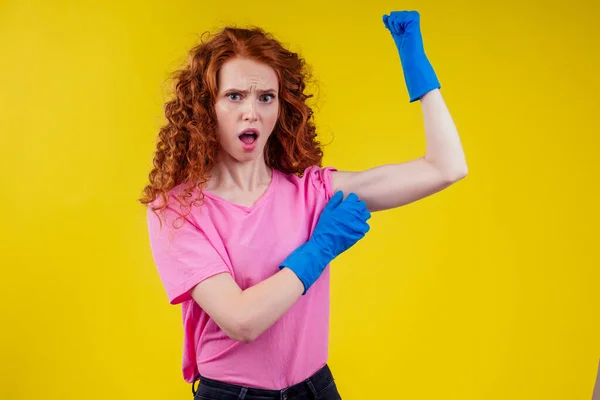 Рыжеволосая кудрявая рыжая женщина показывает тренировочные мышцы рук в студии жёлтая задняя стена — стоковое фото