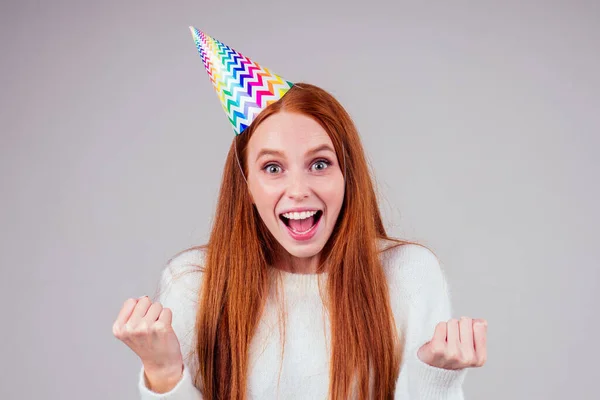 Şaşırmış ve şaşırmış kızıl saçlı kadın doğum günü şapkası takıyor ve elinde stüdyo beyaz arka planda bir sürü hediye kutusu tutuyor. — Stok fotoğraf