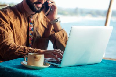 Dizüstü bilgisayarlı Mısırlı mutlu adam Goa 'daki plaj barakasında kahve ya da masala çayı içiyor.