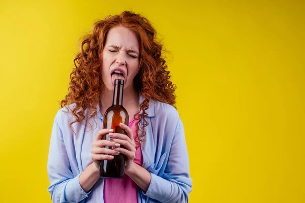 Encaracolado ruiva mulher gengibre beber cerveja e sentir mau humor em csudio fundo amarelo — Fotografia de Stock