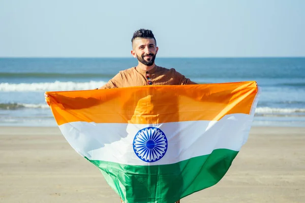 Индийский юноша размахивает индийским триколором под открытым небом рядом с пляжем, концептуальное изображение Дня Республики или Дня независимости — стоковое фото