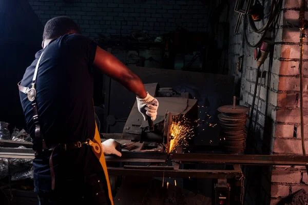 Een knappe Afrikaans-Amerikaanse man die staal smeed naast een oven in een donkere werkplaats. kleine ondernemingen, — Stockfoto