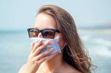 Tropik plajda maske takan bir kadın. Korona virüsünü önleme kavramı