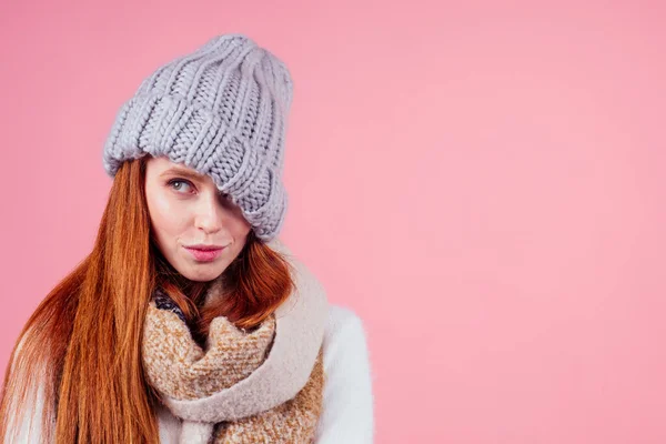 Shy redhead ginger woman putting a knitted hat on his head,hiding eye and open mouth in studio pink background — Stock Photo, Image