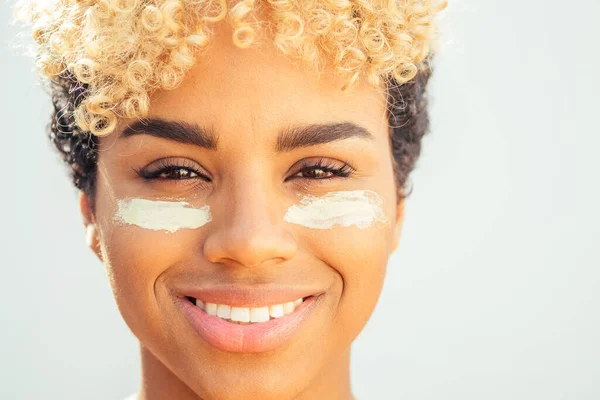 Concept rajeunissant et hydratant. femme brésilienne avec des boucles afro blondes appliquant de l'argile blanche sur une peau parfaite sur fond de studio blanc — Photo